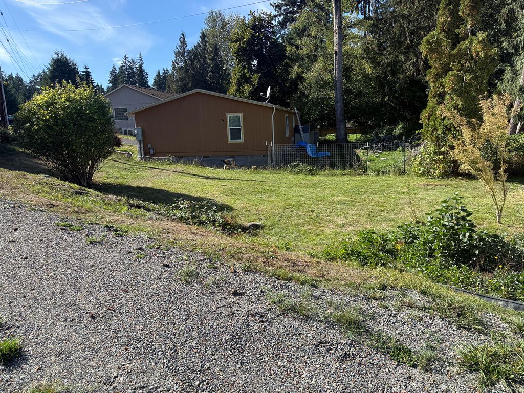 Cut grass and a cleaned-up yard edge along a gravel drive beside a tan house during a pre-sale property cleanup by Black Rabbit Landscaping